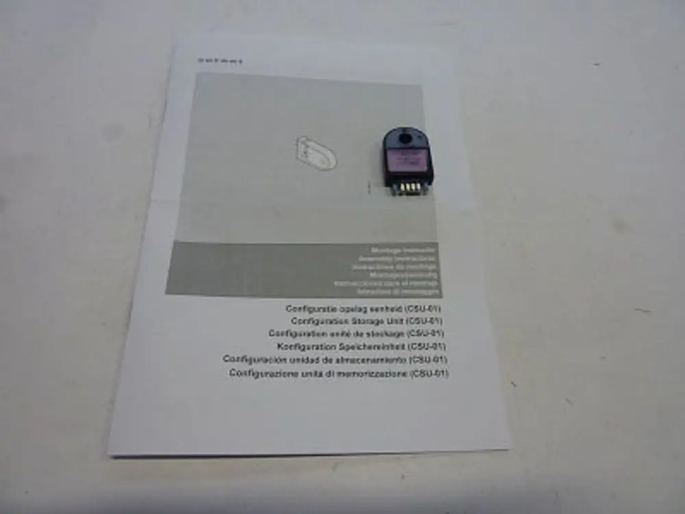 Schwarzes Gerät mit mehreren Pins neben Anleitung in mehreren Sprachen zur Konfiguration von Remeha CSU-01. Anleitung befindet sich auf einem weißen Blatt.